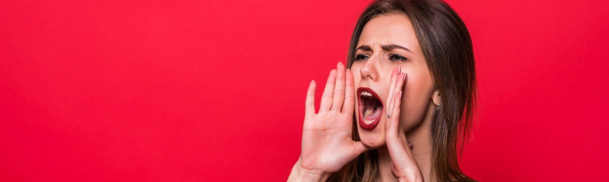 Lady against red wall holding hand up to mouth and shouting 